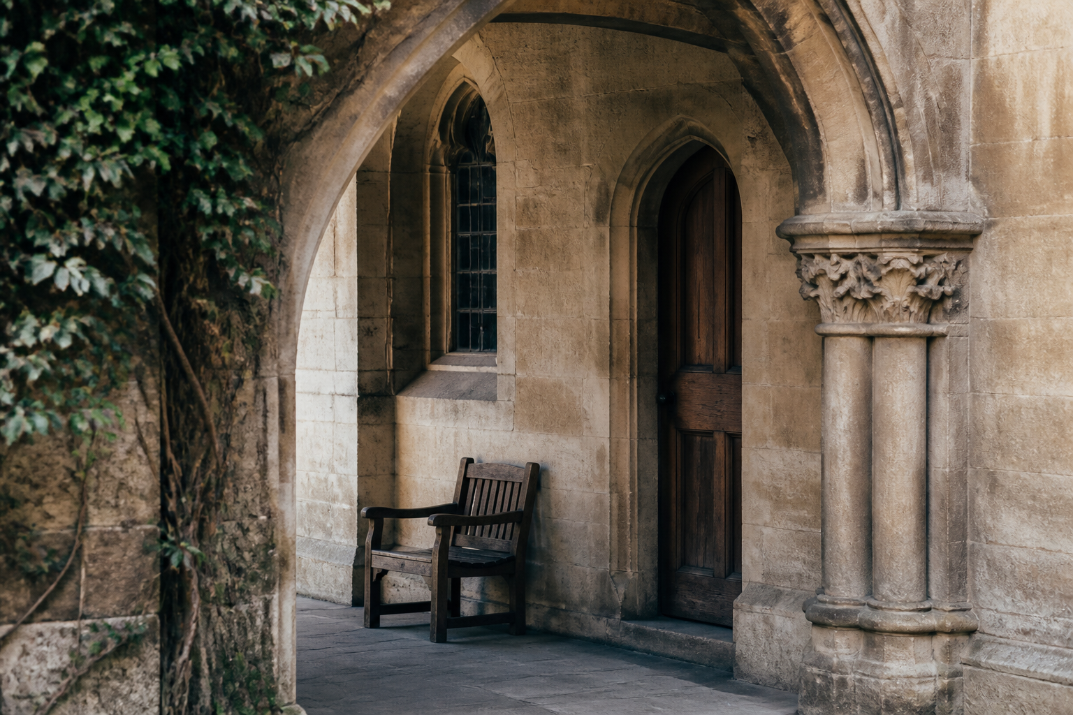 A quiet historic college cloister with limestone arch and wooden chair
